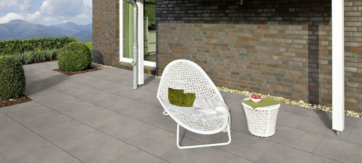 Moderne Terrasse mit großen grauen Fliesen, weißem Loungesessel, Beistelltisch und Blick auf die Berge.