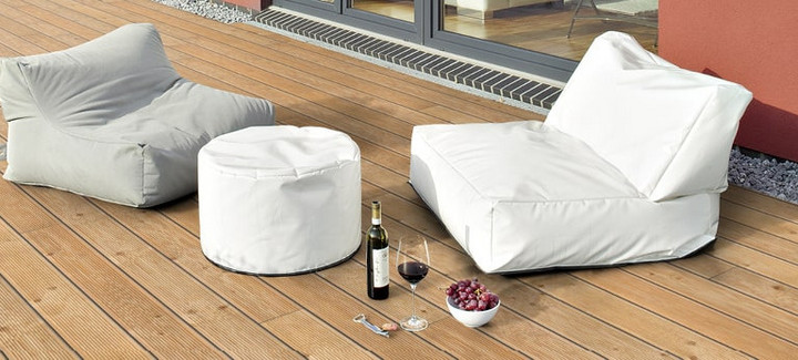 Helle Holzterrasse neben einem Gebäude mit zwei Sitzkissen und dekorativen Elementen.