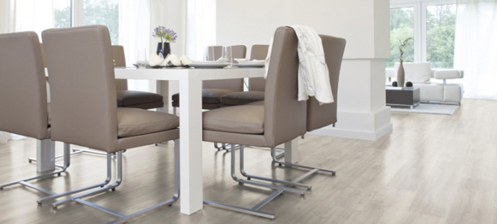 Der Boden im Esszimmer ist mit hellem Vinyl belegt. Dazu gibt es einen großen Esstisch und passende Stühle.