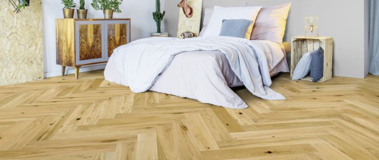 Schlafzimmer mit hellem Fischgrätenparkett ausgelegt.