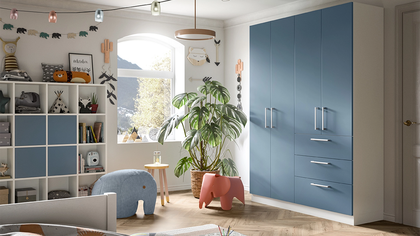 Helles Kinderzimmer mit blauem Kleiderschrank, Regal, Pflanzen und bunten Spielmöbeln.