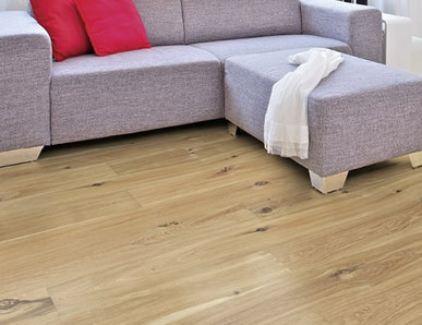 Im Wohnzimmer ist Parkett in Langdielen-Optik verlegt. Dazu passt ein Ecksofa mit bunten Kissen.