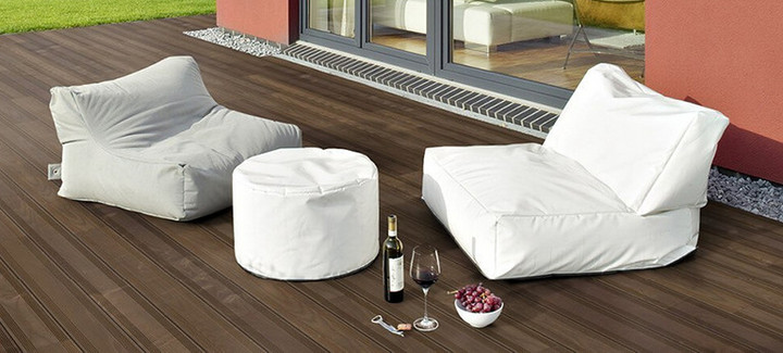 Dunkle Holzterrasse neben einem Gebäude mit zwei Sitzkissen und dekorativen Elementen.