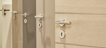 Mehrere nebeneinander angeordnete Türblätter in unterschiedlichen Farbtönen (weiß, holzähnlich, grau) mit integrierten Türgriffen.