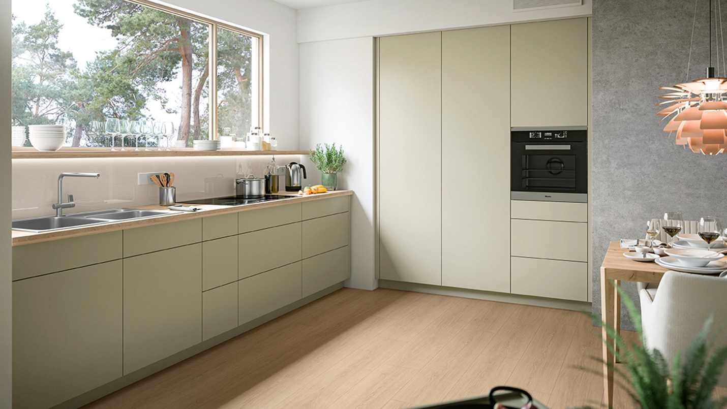 Minimalistische Küche mit matten hellgrünen Fronten, Holzarbeitsplatte, großem Fenster und integriertem Backofen.